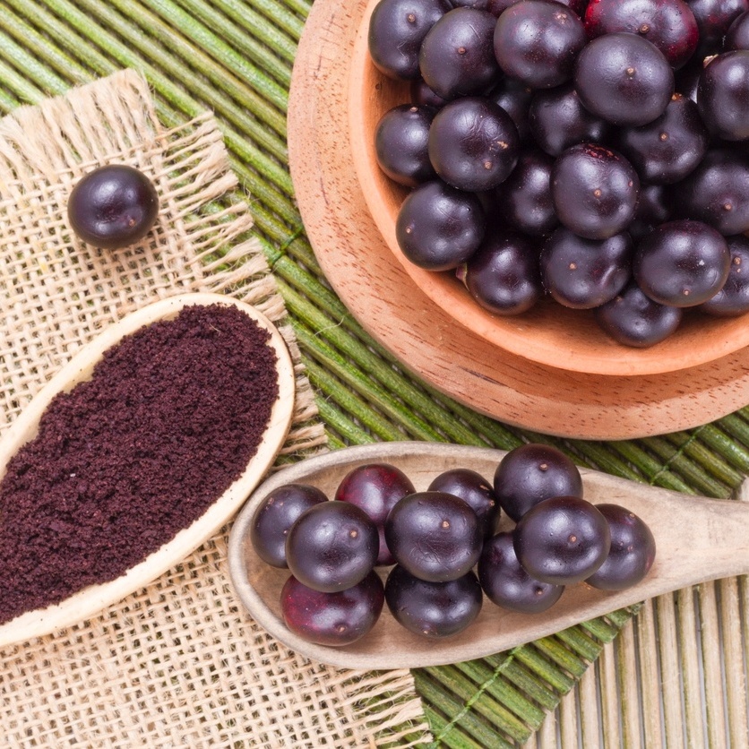 Taças de açaí natural em tigelas de madeira e colher com pó de açaí sobre esteira de palha