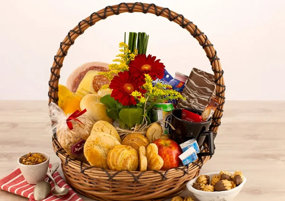 Cesta de pães, frutas, queijos, geleias e flores em um cesto de vime sobre mesa clara