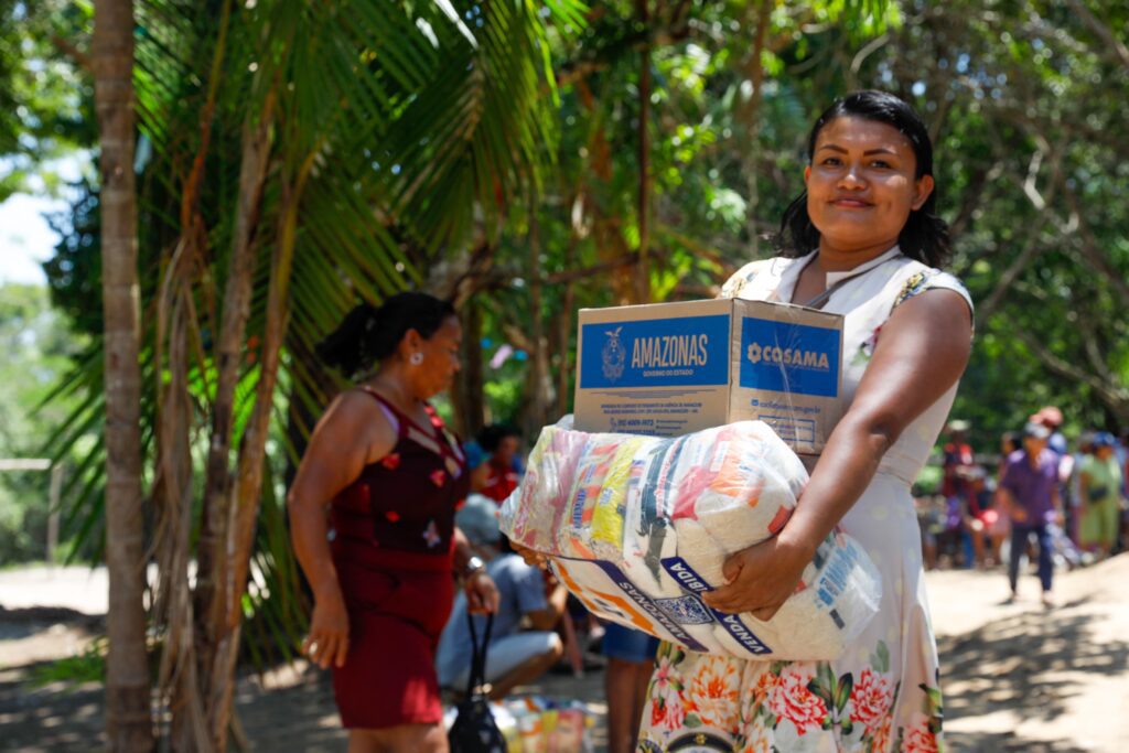 Mulher sorridente carregando caixa de doações da comunidade em ambiente arborizado