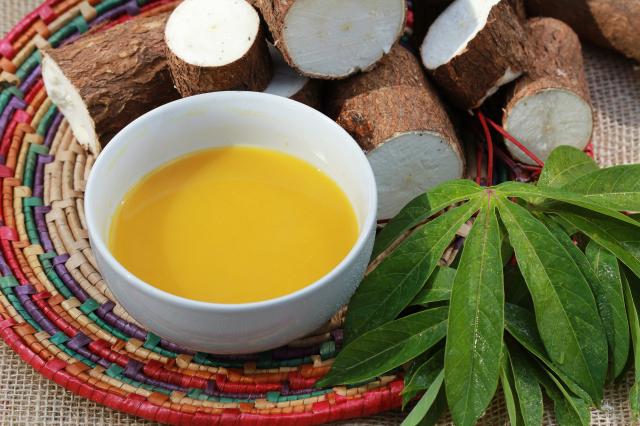 Tigela com tucupi amarelo ao lado de raízes de mandioca sobre esteira de palha